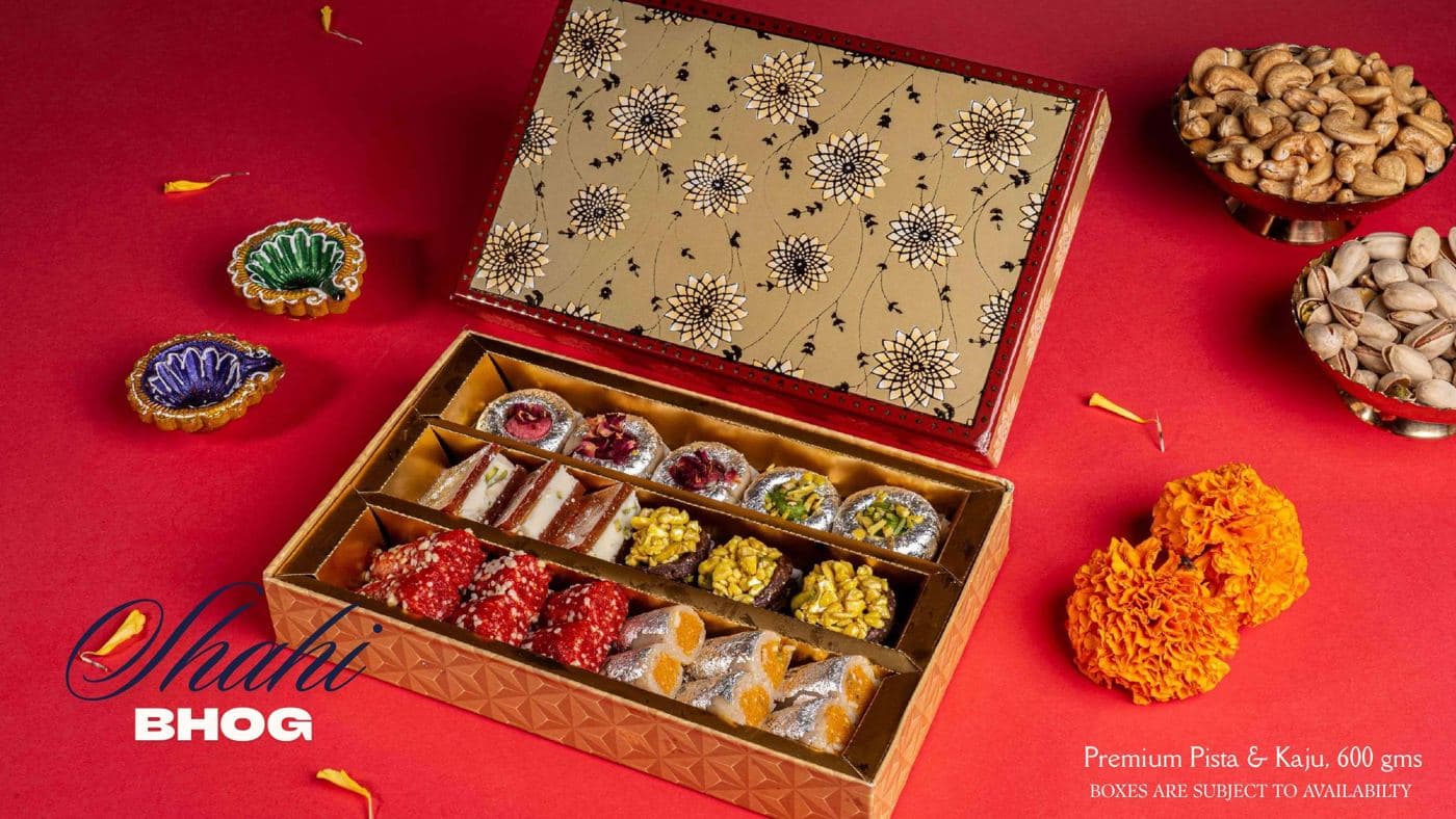 The Shahi Bhog box from Chhappan Bhog, open to show rows of pista and kaju mithai under a gold-printed lid