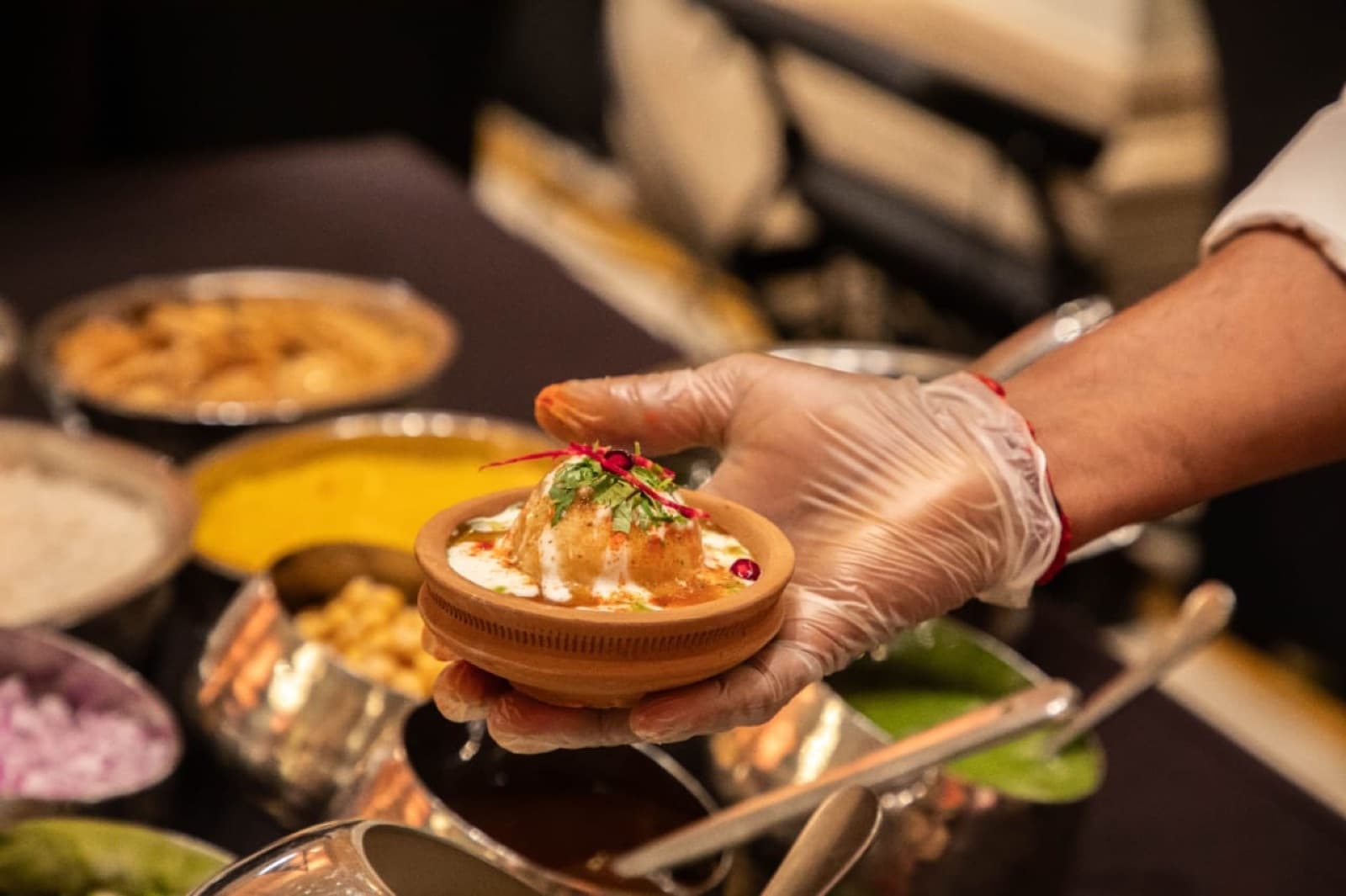 A chef presenting a plated dahi puri in a hand-turned clay bowl